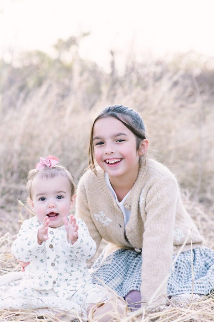 Stylish Houston mom holding toddler surrounded by golden wildflowers during fall