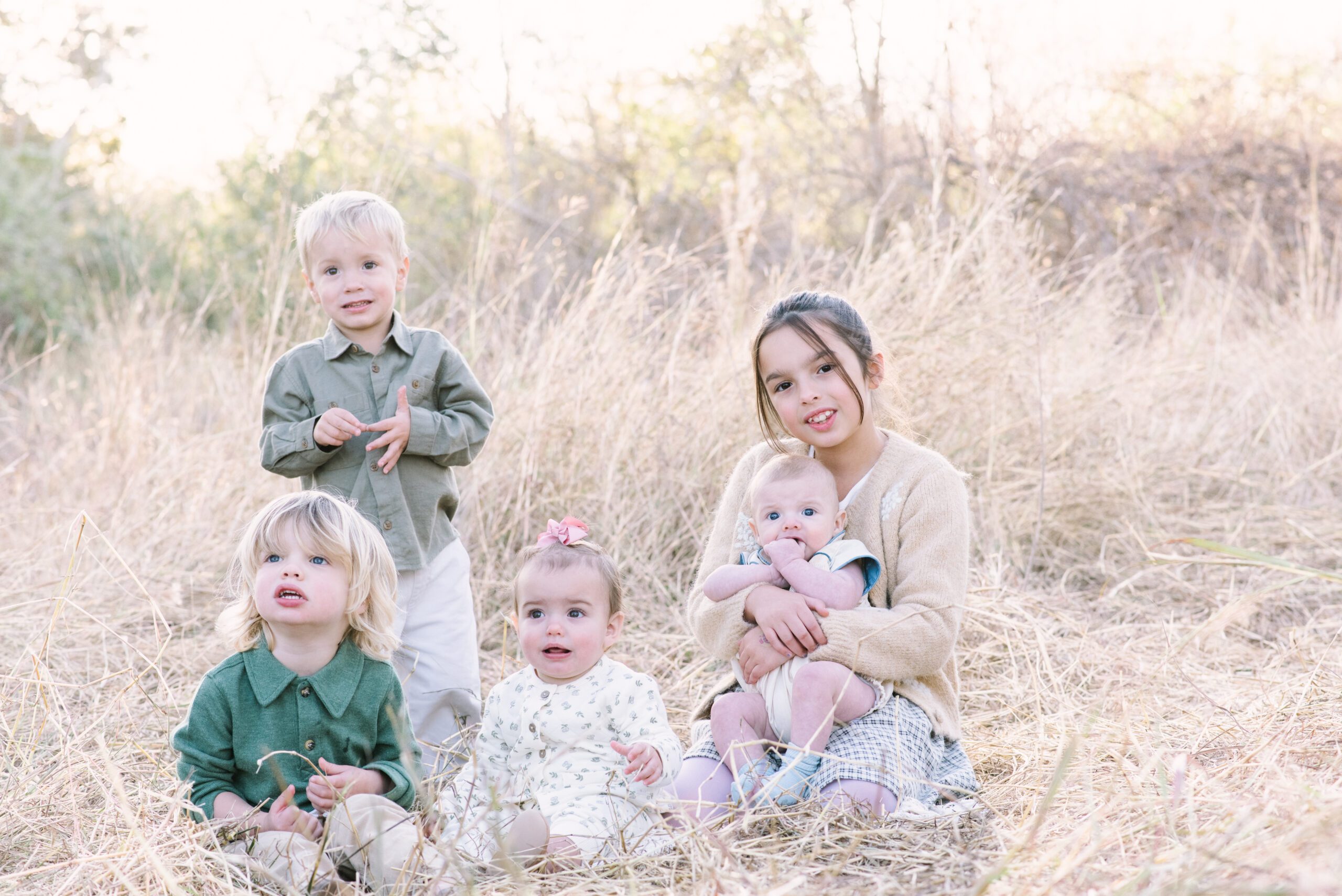 Little cousins sitting in a grassy field in League City at golden hour during fall family photoshoot near Houston, Texas