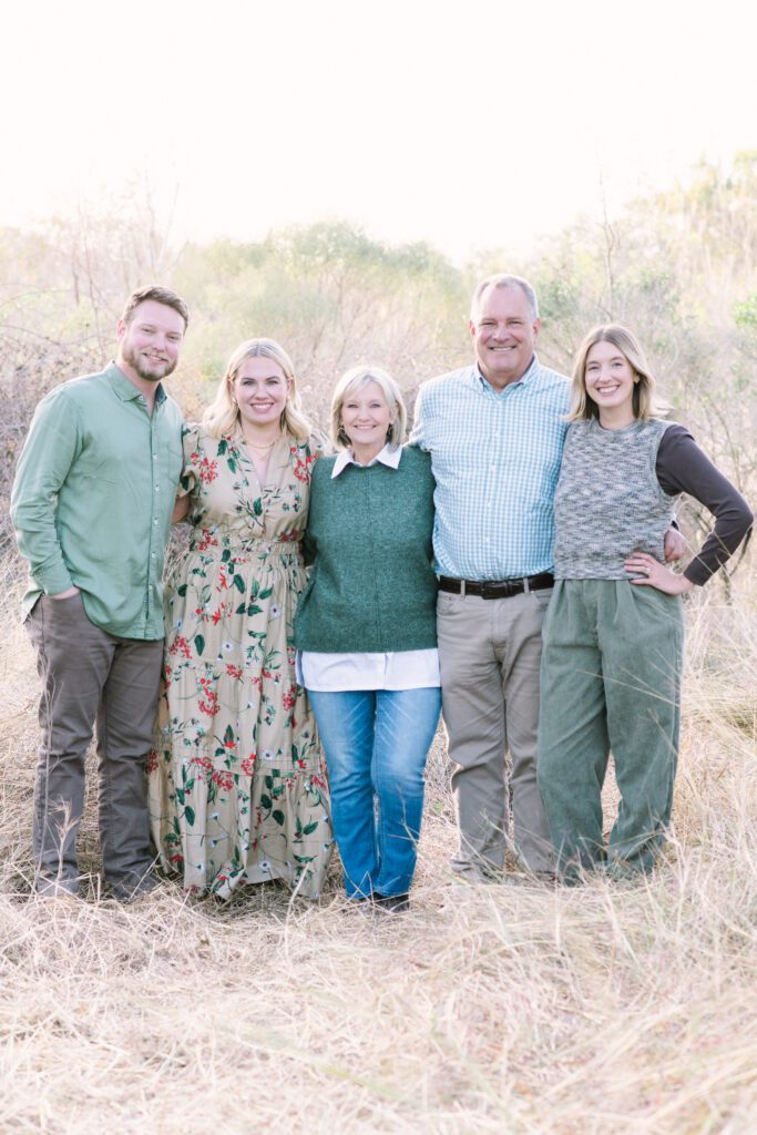 Extended family joyfully standing in tall golden grass in a Houston field during fall